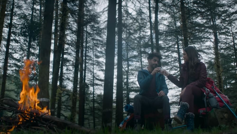 Aparshakti Khurana and Jasmin Bhasin are sitting near the bonfire in a forest and having a cup of tea. The picture is screen grab from Hum dono lyrics video from Arko latest.